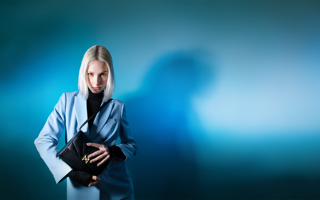 Modèle féminin en costume bleu ciel, tenant à la main le sac MAES M1_01 en coloris noir
